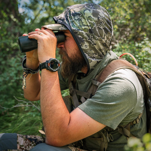 man looking through binoculars wearing a "Western Land Camo" hood by Kinich Sun Hoods