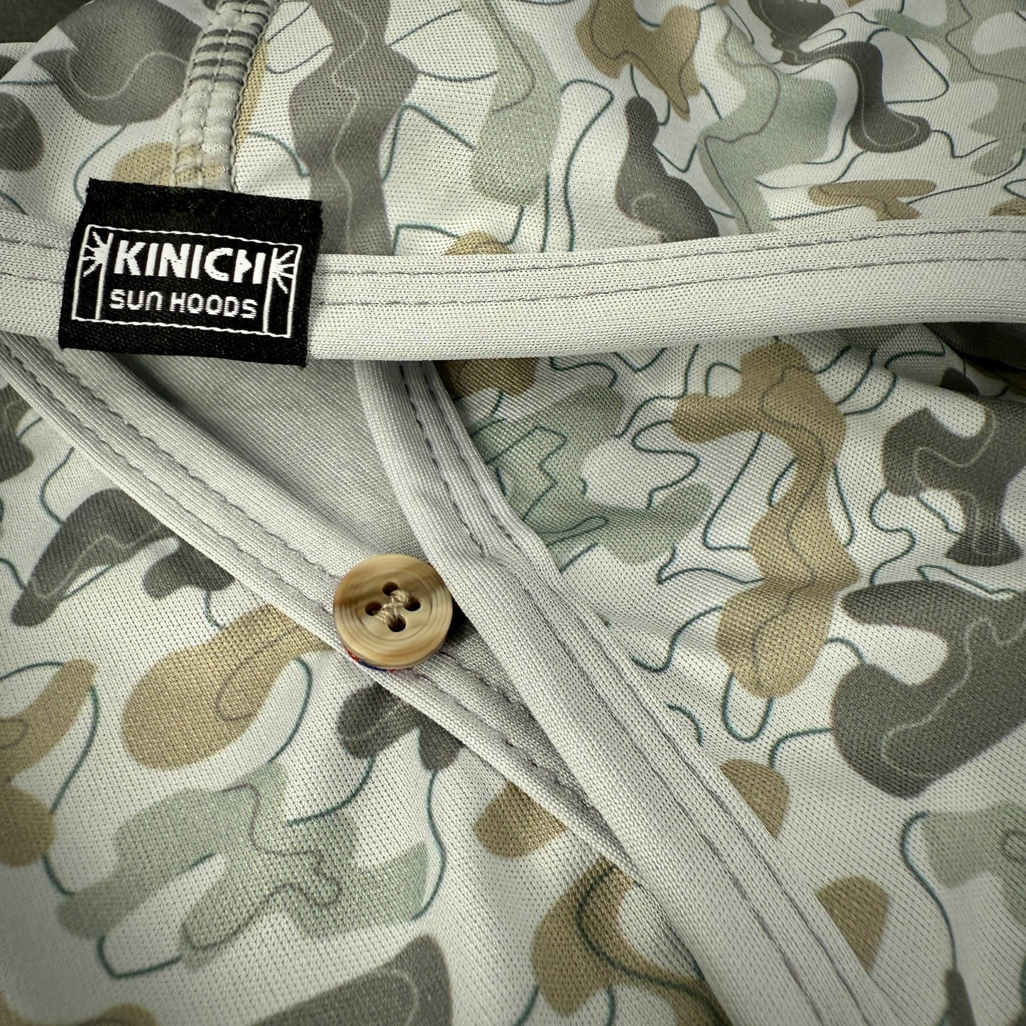 Camouflage-patterned fabric with a button and Kinich Sun Hoods label.