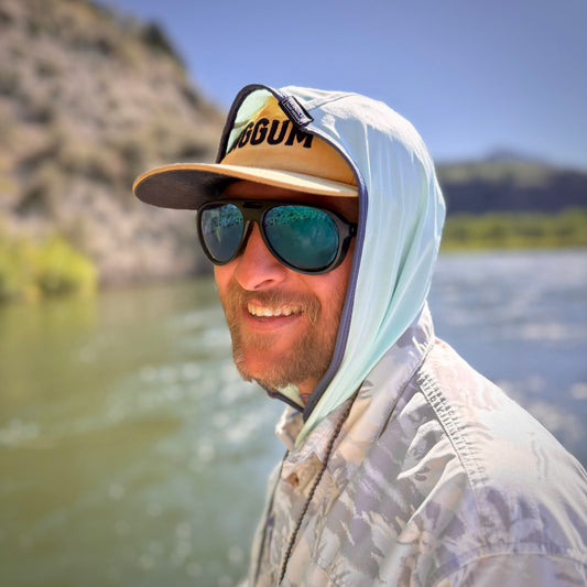 Man wearing sun protective hood standing by a body of water.