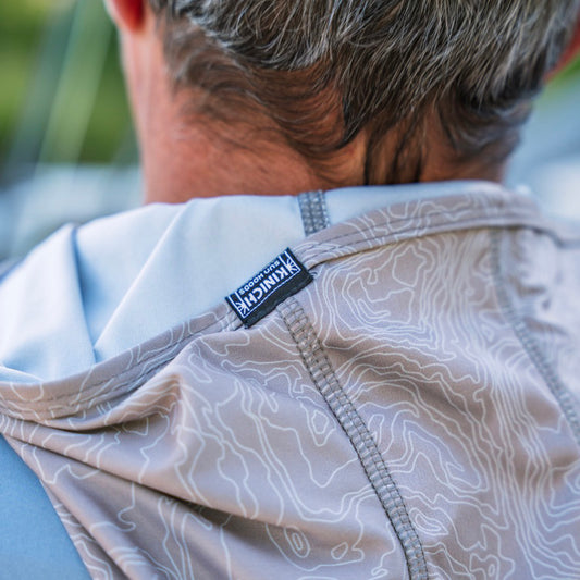 Close-up back view of a person wearing a Grey sun hood with a topographic contour pattern and a visible black and white 'Kinich' brand tag near the collar.