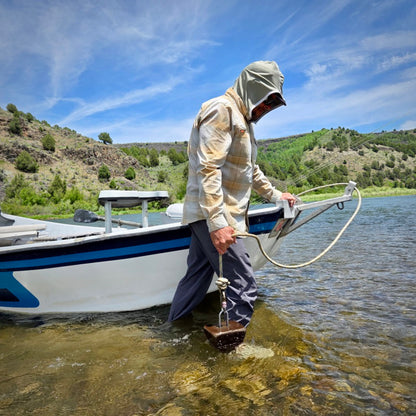 Fishing guid walking a boat in a river with a UPF 50+ olive hood on