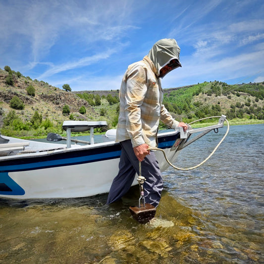 Fishing guid walking a boat in a river with a UPF 50+ olive hood on